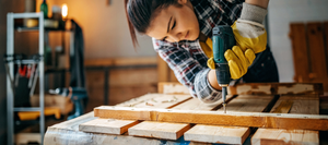 A woman using a power drill on a wood project.