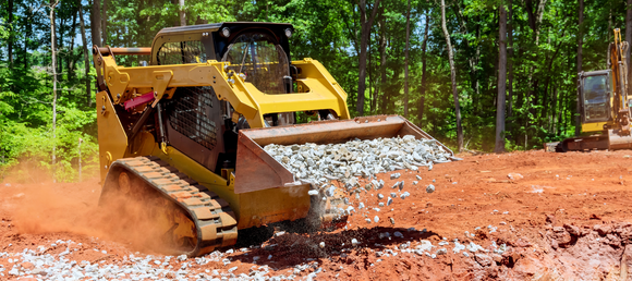 A skid steer carrying gravel in it's in bucket.